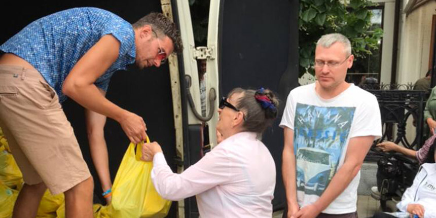 Man handing woman yellow bag of aid items